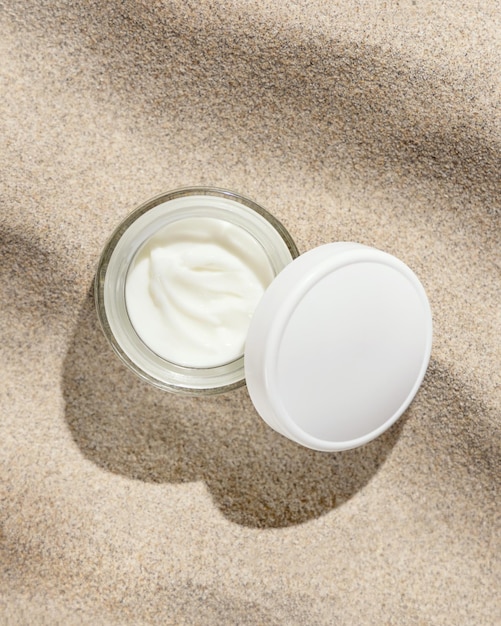 Opened cream jar with white lid on beige sand top view hard light Cosmetic mockup