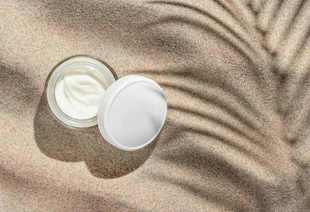 Opened Cream jar with white lid on beige sand top view palm leaf shadow Mockup