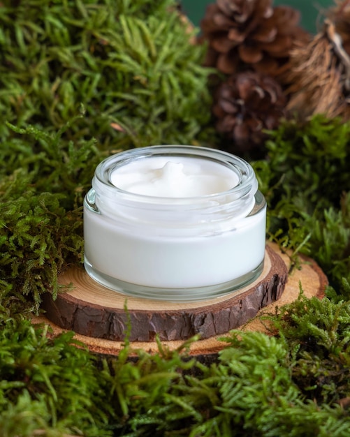 Opened glass jar full of cream on wooden piece between green moss closeup mockup