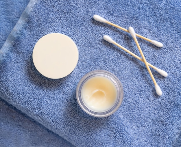 Opened lip balm jar with blank lid near cotton swabs on folded blue towels mockup