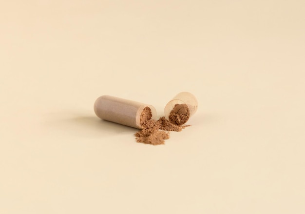 Opened Medical capsule to show brown powder on light beige close up Dietary supplements