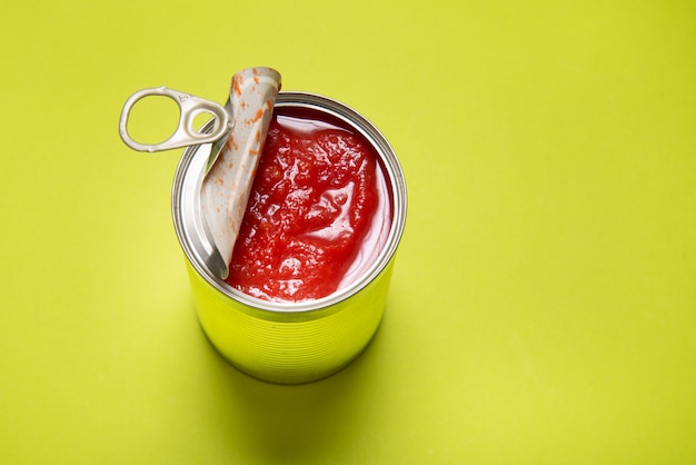 Photo opened tin can with canned tomatoes, on green background