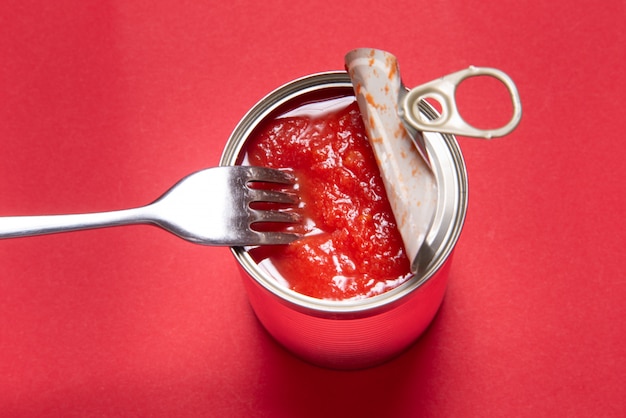 Photo opened tin can with canned tomatoes, on red background