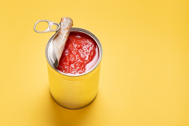 Photo opened tin can with canned tomatoes, on yellow background