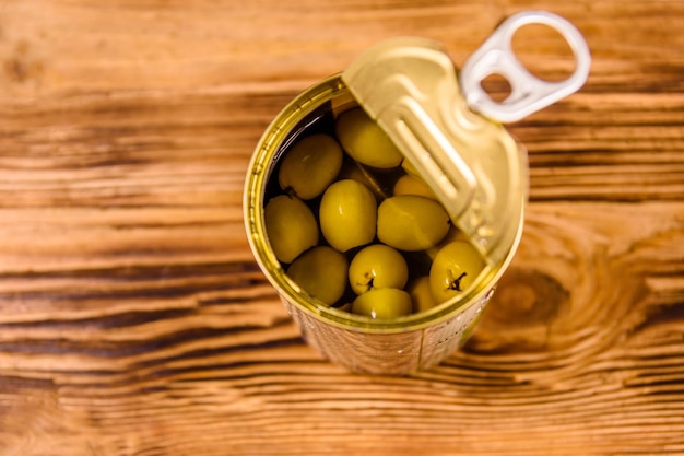 Opened tin can with green olives on wooden table