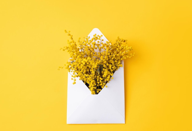 Opened white envelope with yellow mimosa flowers on yellow background mockup design