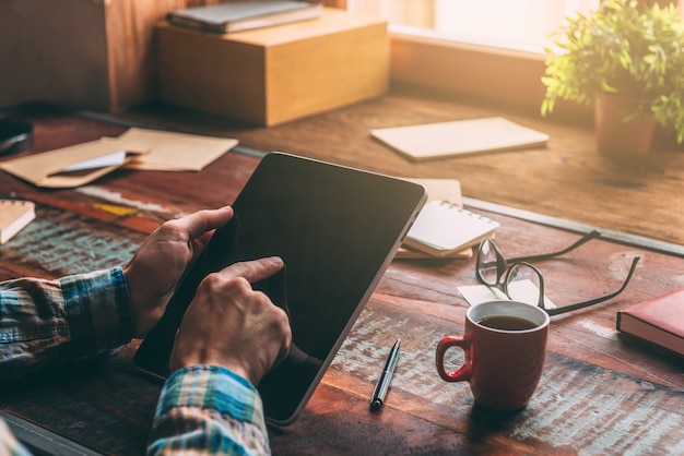 Opening the world with single touch. Close-up image of man holding digital tablet with copy space while sitting at the rustic wooden table