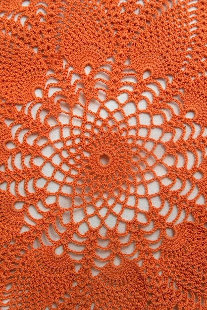 Openwork napkin for decor on white background Bright orange crocheted product Knitted lace pattern Vertical frame