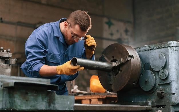 Photo operating the automatic machine factory worker in blue uniform is indoors