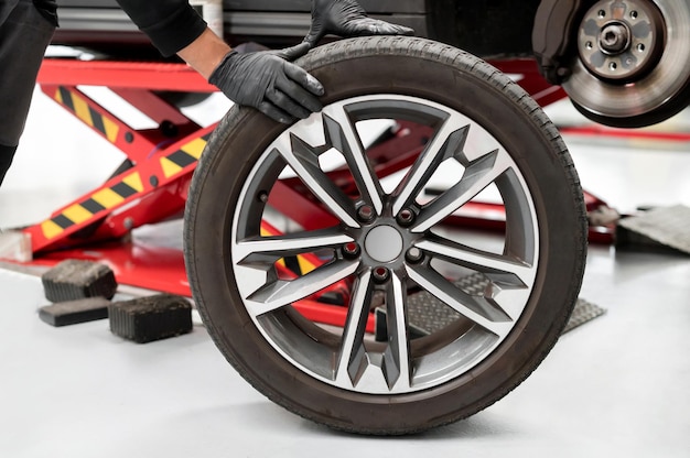 Operator in gloves supporting car with wheel in workshop