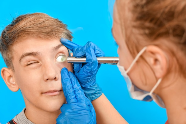 An ophthalmologist examines a teens eye and shines a flashlight into his eye