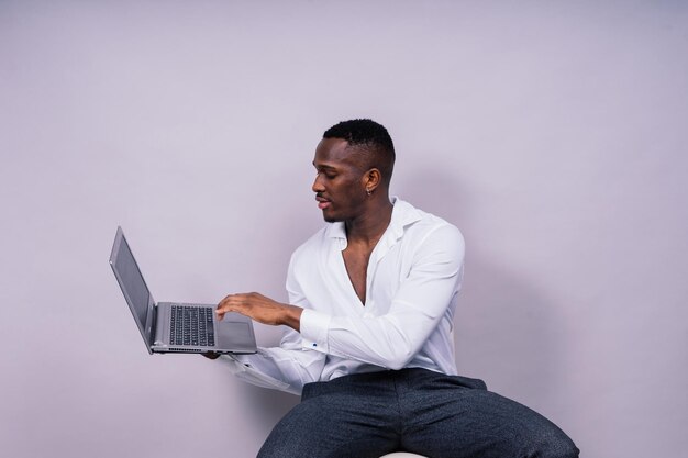 Optimistic africanamerican male student in casual shirt using laptop pc isolated