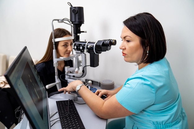 Optometry concept Beautiful young woman is having eyes examined by an eye doctor Experienced doctor is diagnosing female patient Closeup