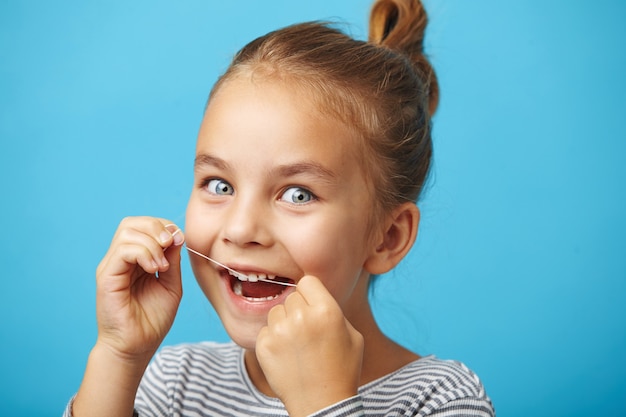 Oral hygiene and health care. Smiling child girl use dental floss white healthy teeth.