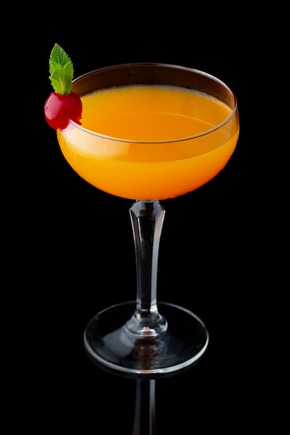 Orange alcohol cocktail with mint and cherry isolated on black