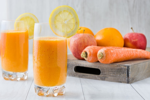 Orange, apple and carrots smoothie on white wooden table