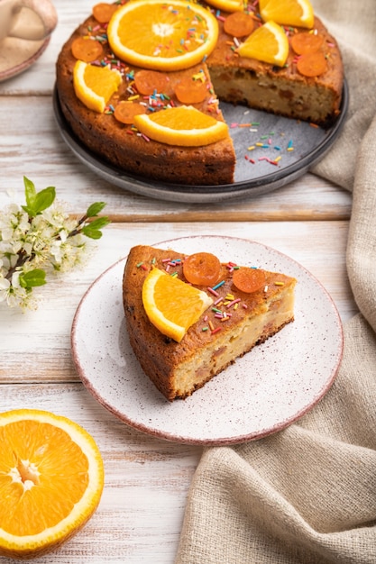 Orange cake and a cup of coffee on a white wooden table and linen textile. Side view, close up.