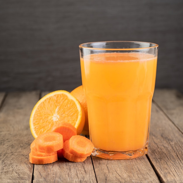 Orange and carrot juice in a glass with fruits over wooden table.