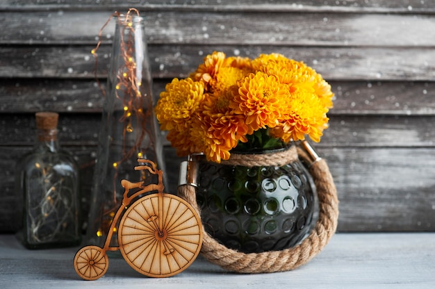 Orange chrysanthemum flowers and wooden bike on rustic table.