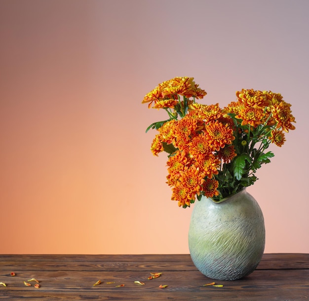 Orange chrysanthemums in vase on wooden background