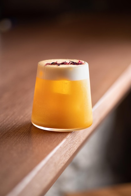 Orange colored cocktail with white foam on brown table