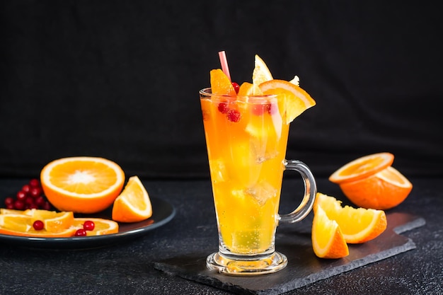 Orange cranberry fizzy cocktail in a glass and fruits next to it on a dark background Homemade mocktail