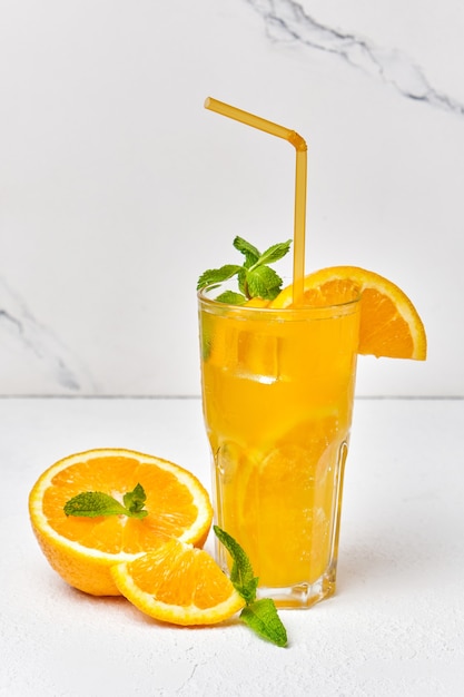 Orange drink with mint and ice in glass close up on light surface