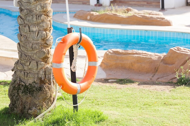 Orange emergency lifebuoy hanging on fence near pool on vacation at the hotel with copy space