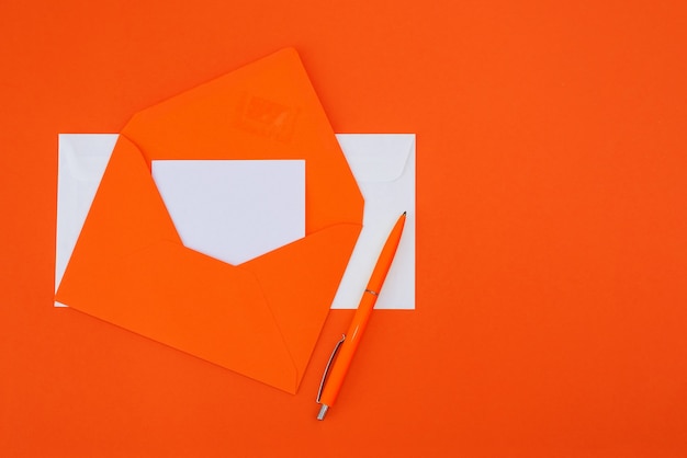 Orange envelope with a pen on an orange background. Copy space. View from above. Flat lay.