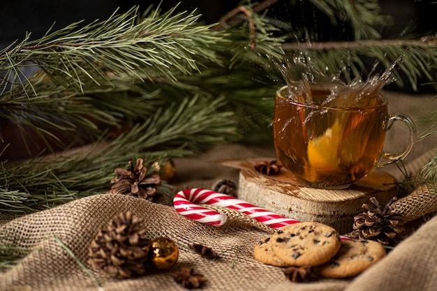 orange falls into tea and splashes around, next to cookies and lollipop on a Christmas tree and cones.