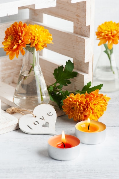 Orange flowers in glass pot on rustic table. Greeting card with lit candles and heart