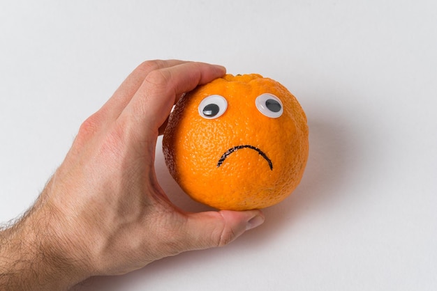 Orange fruit character. Orange with eyes and sad smile in man hand. Food with Funny Faces.