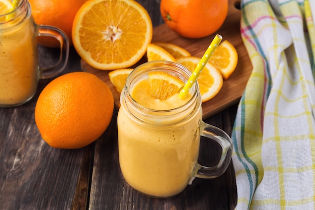 Orange fruit smoothie in the glass jar with fresh orange slices on rustic wooden background