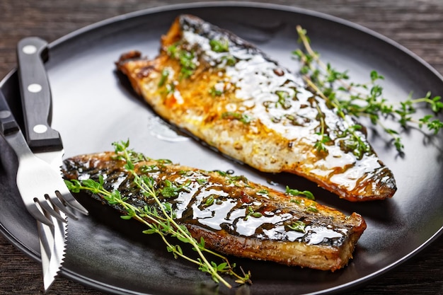 Orange glazed fried mackerel fillets with spices and thyme on a black plate