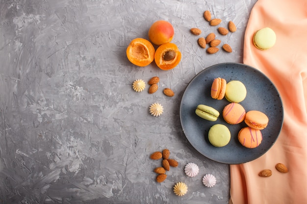 Orange and green macarons or macaroons cakes on blue ceramic plate on a gray concrete background, top view.