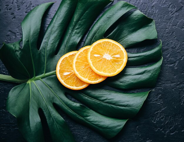 An orange on green tropical leaf. Monstera houseplant on black background. Eco friendly photo.