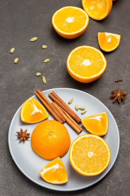 Orange halves and cinnamon sticks on gray plate. Star anise and chopped oranges on table. Black background. Top view