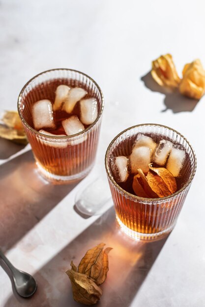 Orange healthy cold beverage cocktails decorated with physalis berry on marble background Drink Photo with hard light and clear shadows Autumn party concept