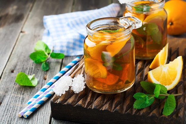 Orange iced tea with mint leaves in a glass jar on the old wooden background. Selective focus.