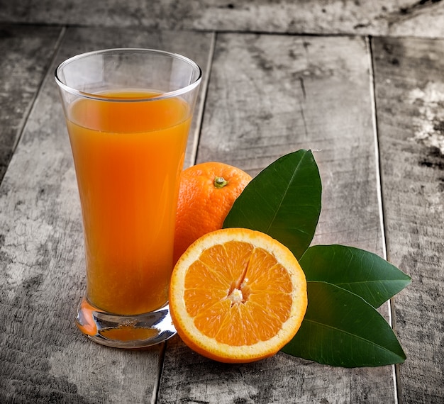 Orange juice glass and fresh oranges on wood