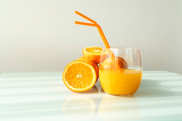 Orange juice in a glass surrounded by natural oranges with a natural sun light white background