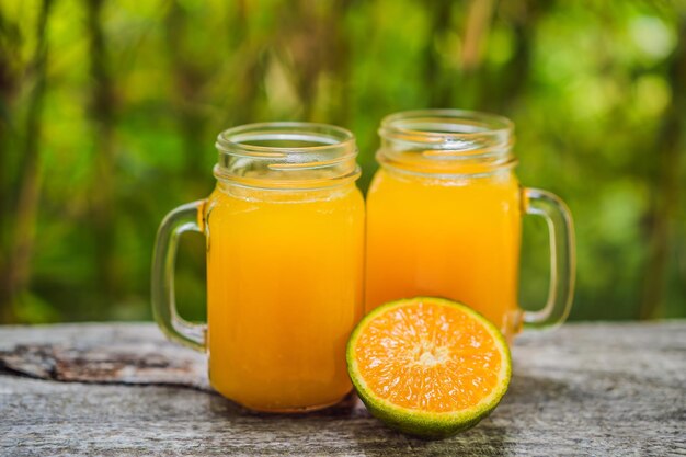 Orange juice and oranges with green peel on a wooden background