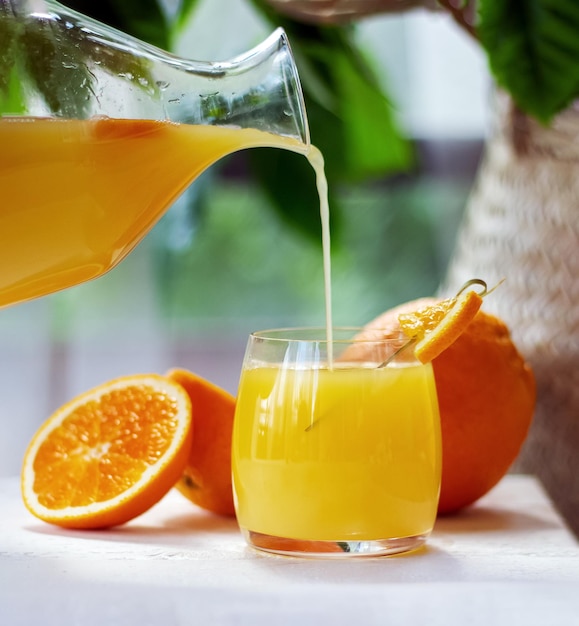 Orange juice pouring from pitcher into glass Healthy citrus drink Summer freshness concept