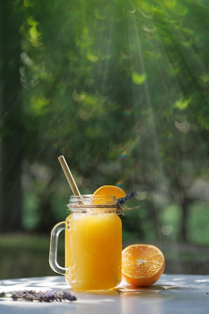 Orange lemonade in a mug on table against the background of greenery in sunlight