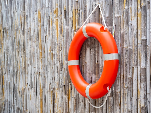 An orange lifebuoy safety ring hanging on bamboo fence wall background with copy space Rescue equipment Lifesaver Safety concepts