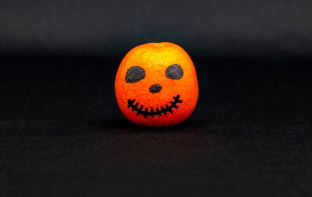 An orange mandarin painted like a halloween pumpkin