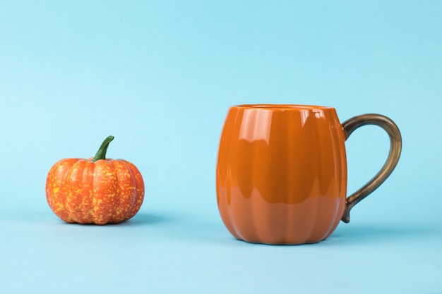 An orange mug and a pumpkin figurine on a blue background. Pumpkin style.