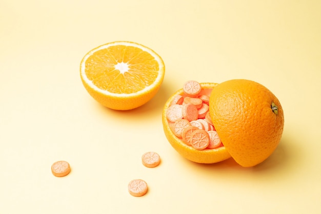 Orange peel filled with vitamin C pills and a half of an orange on a yellow