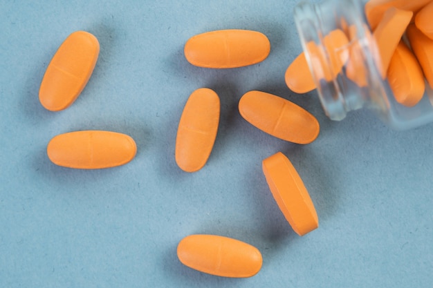 Orange pills pouring out of the glass jar on blue