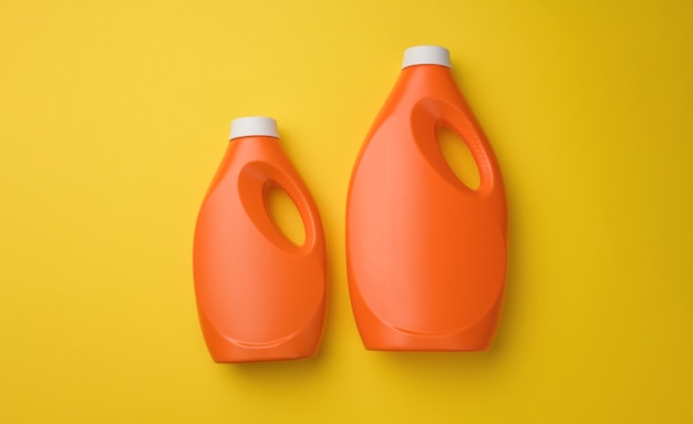 Orange plastic bottle for liquid washing powder on yellow background, top view